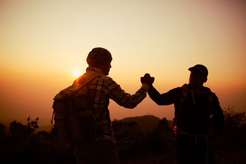 Zwei Wanderer schlagen bei Sonnenaufgang auf dem Gipfel ein.
